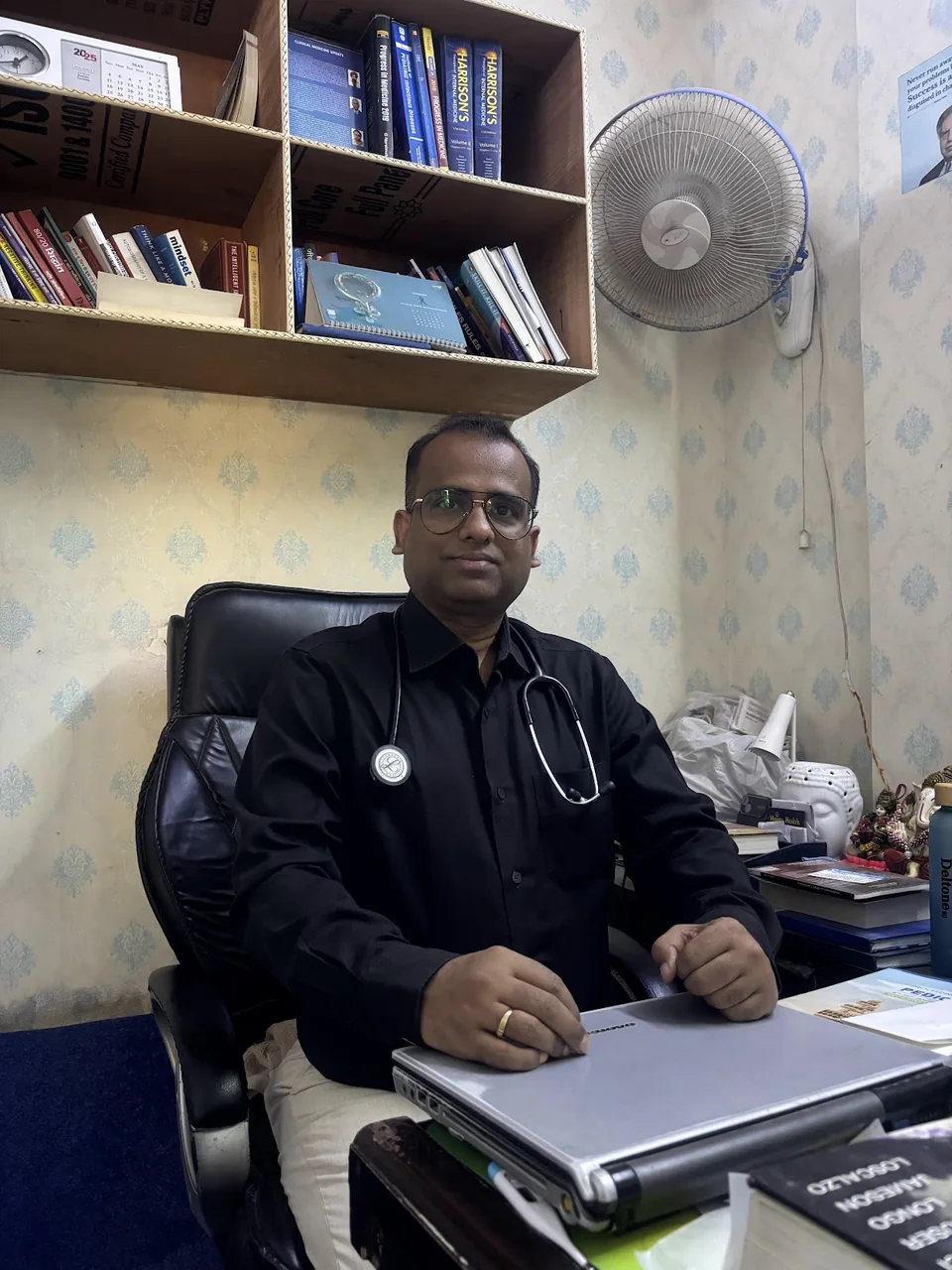 Dr. Rajesh Kumar Raman at his desk beside a shelf of medical textbooks